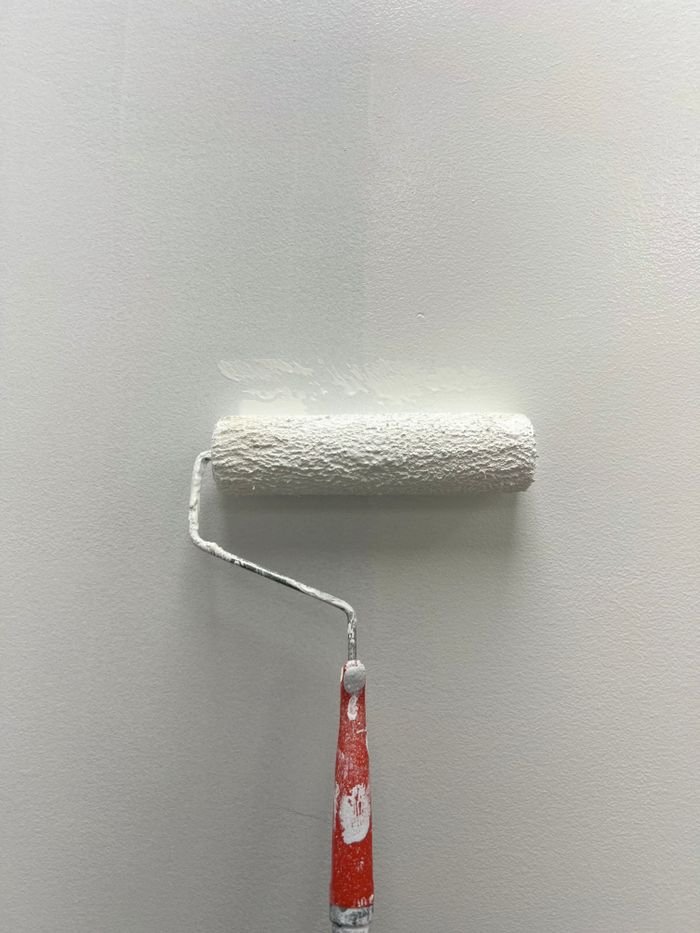 A white paint roller applying new coat on a smooth gray wall indoors.