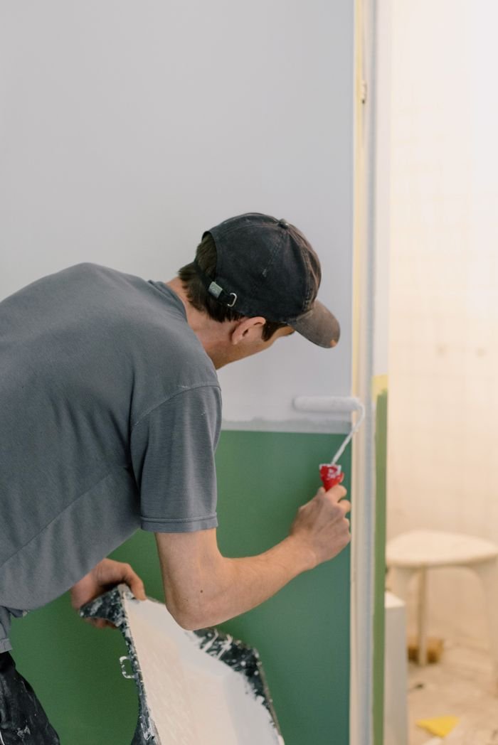 Back view of unrecognizable male in cap holding roller while painting walls in room